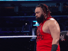 a wrestler in a red tank top stands in a ring