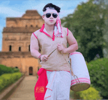 a man wearing sunglasses and a headband holds a drum in front of a building