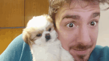 a man holding a small brown and white puppy