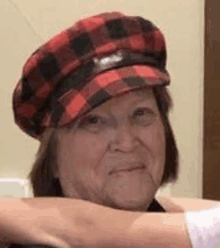 an elderly woman wearing a red and black plaid hat is sitting in a chair .