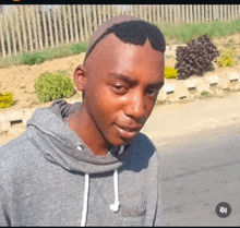 a young man wearing a gray hoodie has a shaved head and sunglasses on