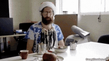 a man with a beard wearing a santa hat is sitting at a table with a bowl of food .