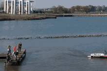 a group of people are standing on a dock overlooking a body of water with a building in the background