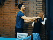 a man and a woman are standing next to a brick wall