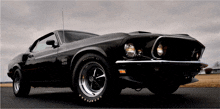 a black mustang is parked on a road with goodyear tires