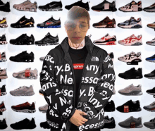 a man wearing a supreme jacket is standing in front of a wall of sneakers