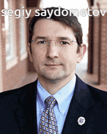 a man in a suit and tie is standing in front of a brick building with the caption segiy saydometov