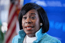 a woman wearing a blue jacket and earrings smiles