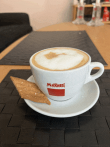 a cup of cappuccino sits on a saucer with a piece of cookie on it