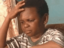 a young boy is sitting on a couch holding his head with his hand .