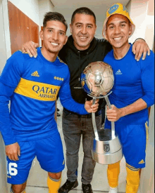 a man holding a trophy next to two soccer players wearing qatar airways shirts