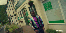 a man in a sequined jacket is standing in front of a store that sells newspapers magazines and grocery items