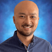 a bald man with a beard wearing a blue shirt is smiling .