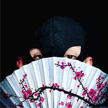 a person wearing a black mask holds a fan with pink flowers on it