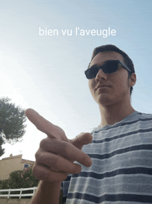 a man wearing sunglasses is pointing at the camera with the words bien vu l' aveugle behind him