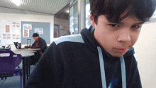 a boy in a black hoodie looks at the camera in a classroom