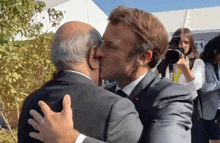 a man in a suit kisses another man in front of a woman taking a picture