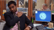 a man in a suit and tie is sitting at a desk in front of a computer with the new york seal on the screen .