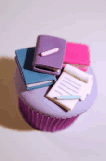 a purple cupcake with a stack of books on top of it