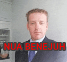 a man in a suit and tie stands in front of a sign that says nua benejoh