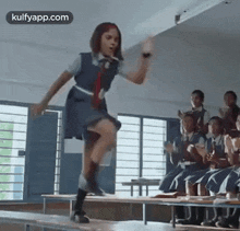 a girl in a school uniform is dancing in a classroom while a group of children sit on benches .