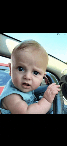 a baby is sitting in the driver 's seat of a car and looking at the camera