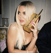 a woman in a black dress is holding a gold purse that looks like a cell phone