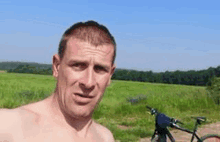 a shirtless man is standing in front of a bicycle in a field .