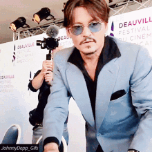 a man in a suit and sunglasses stands in front of a sign that says deauville festival du cinema america