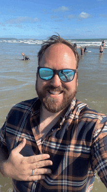 a man wearing sunglasses and a plaid shirt smiles at the camera