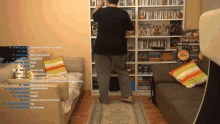 a man in a black shirt is standing in front of a couch in a room with a lot of books on shelves