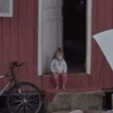 a little girl is sitting on the steps of a red house