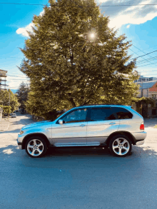 a silver bmw is parked in front of a large tree