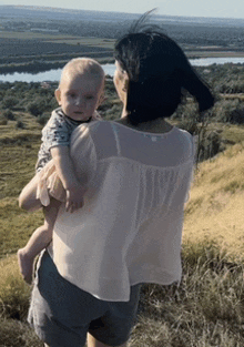 a woman is holding a baby in her arms on a hill