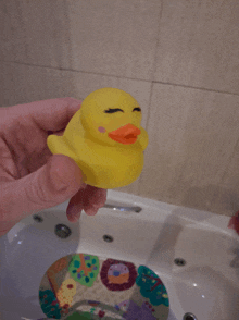 a person holding a yellow rubber duck over a bathtub