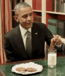 a man in a suit and tie is sitting at a table with a plate of cookies and a glass of milk