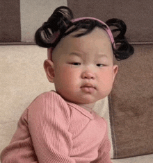 a baby girl wearing a pink shirt and a pink headband is sitting on a couch .