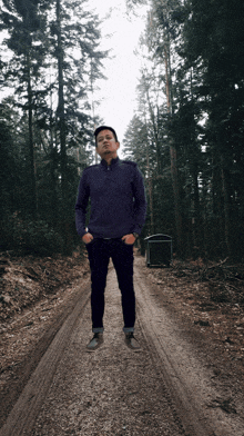 a man in a purple sweater stands on a dirt road