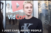 a man wearing a black shirt with the letter k on it is standing in front of a vidcon sign