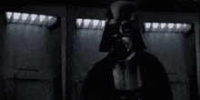 darth vader is standing in front of a door in a dark room in a black and white photo .