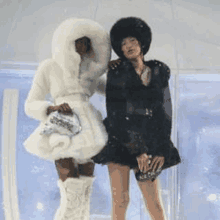 two women are standing next to each other and one is wearing a fur coat and the other is wearing a black dress .