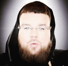 a man with a beard and glasses is wearing a black hooded jacket .