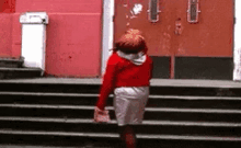 a young girl in a red jacket and white skirt is walking down stairs .