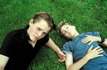 two men are laying in the grass together .