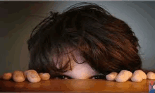 a person is peeking over a wooden table with their eyes visible .