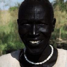 a man with black paint on his face is smiling and wearing a necklace .