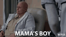 a woman with a bald head sits in a chair with mama 's boy written below her