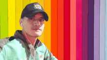 a man wearing a hat and earphones is standing in front of a rainbow wall .