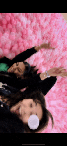 two women are laying on a pink wall with bubbles in their mouths