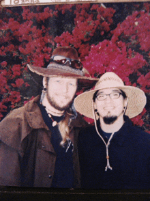 a man wearing a cowboy hat and glasses poses with another man